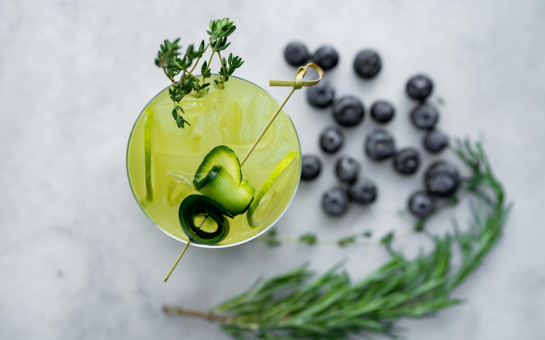 A cocktail garnished with cucumber and thyme on a marble surface